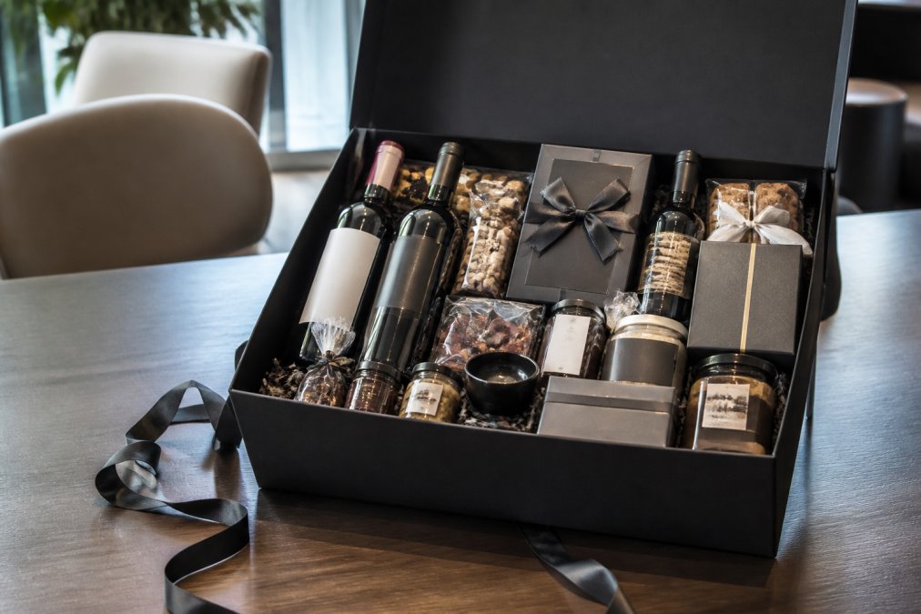 Luxury branded gift hamper opened to reveal gourmet items, wine bottles, and custom branding elements, displayed on a modern table in a contemporary corporate setting