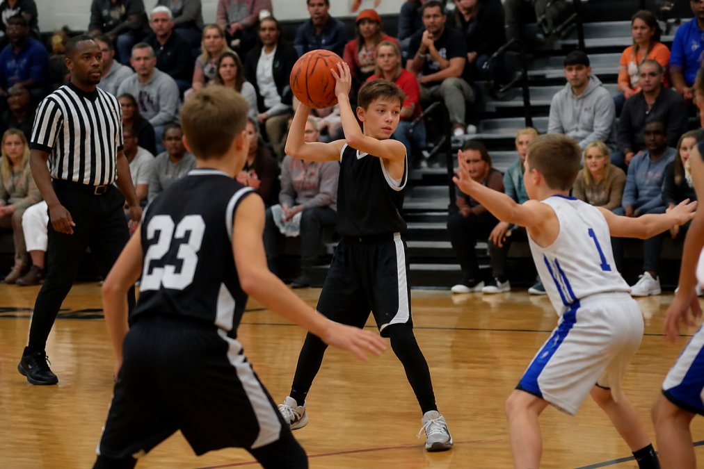Young basketball players in a competitive game, passing and shooting under game conditions with a referee officiating, showing intense focus and team coordination in a gymnasium with spectators