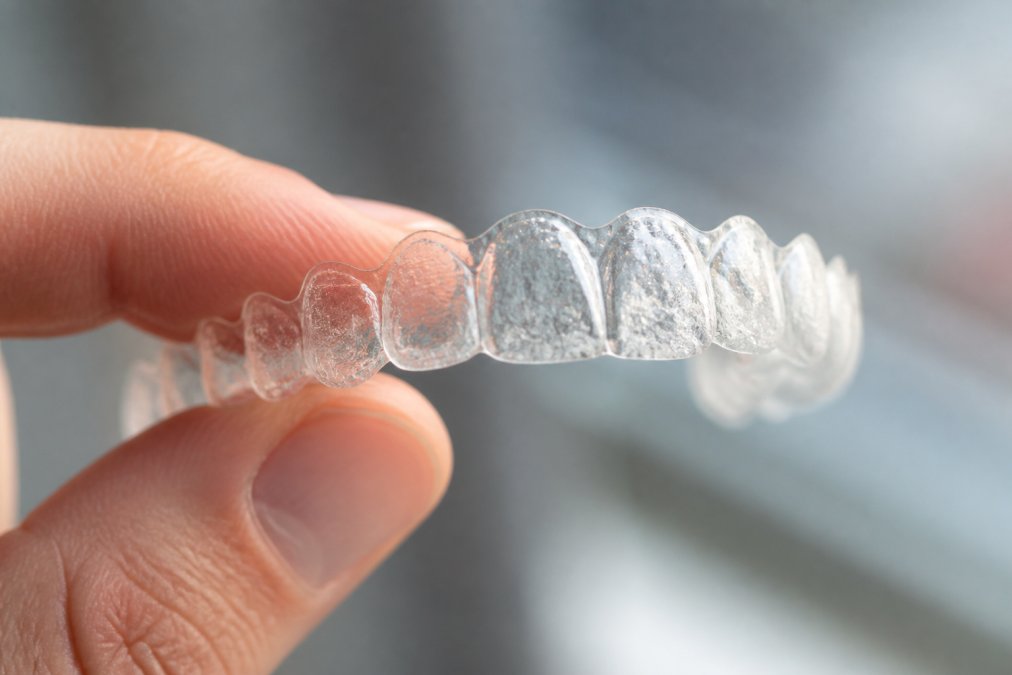 Close-up of a dental aligner being held between fingers, showing surface detail and light reflection emphasizing the transparent material texture and microscopic surface imperfections