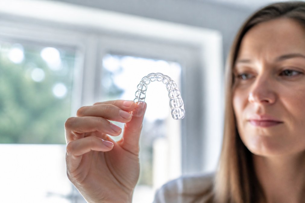 Person hält eine transparente Zahnschiene gegen das Licht und inspiziert sie auf Klarheit und Integrität nach der Reinigung