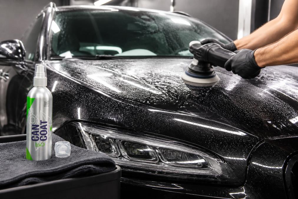 Detailer die een auto polijst met een orbitale polijstmachine, waarbij water en polijstresidu zichtbaar zijn op het lakoppervlak in een goed verlichte garage