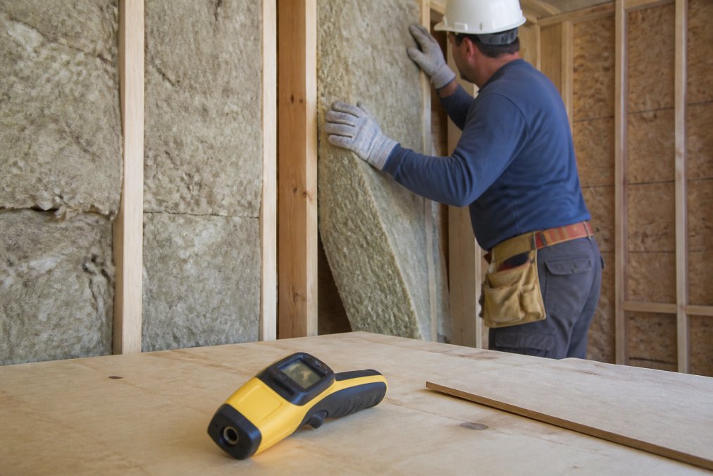 Builder installing thick wall insulation for a zero energy design project with an infrared thermometer nearby