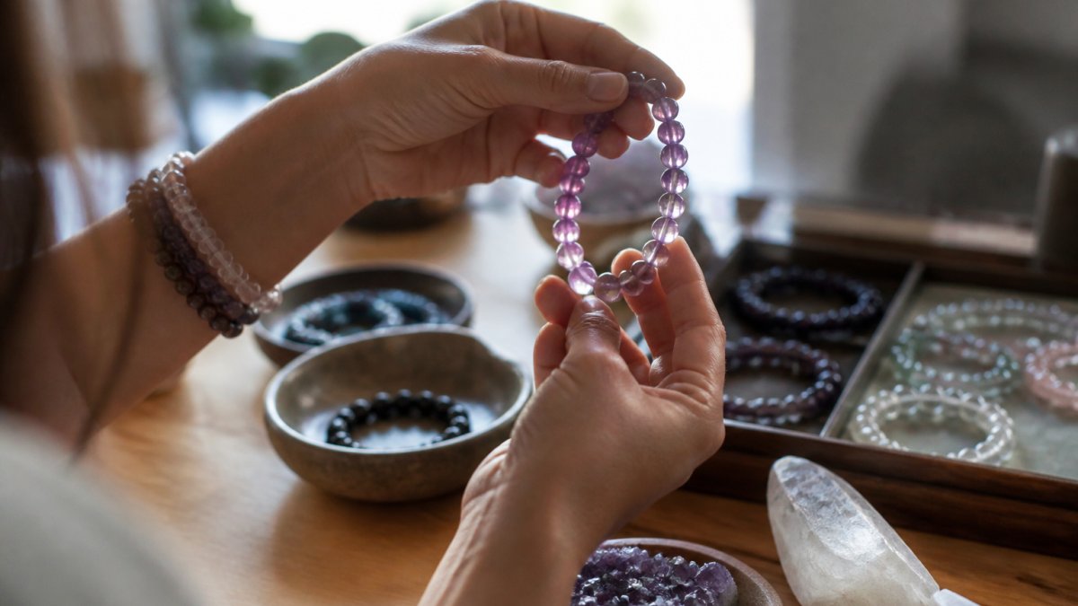 Close-up van handen die voorzichtig een edelsteenarmband onderzoeken tegen het licht, waarbij de glans en kleurgradiënten van de natuurlijke kralen zichtbaar zijn