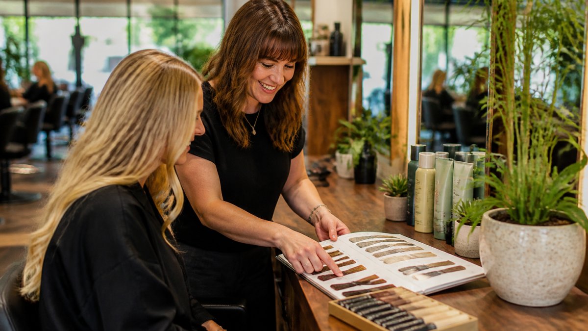 Stylist and client reviewing color swatches at a bright, modern Aveda salon station filled with natural light