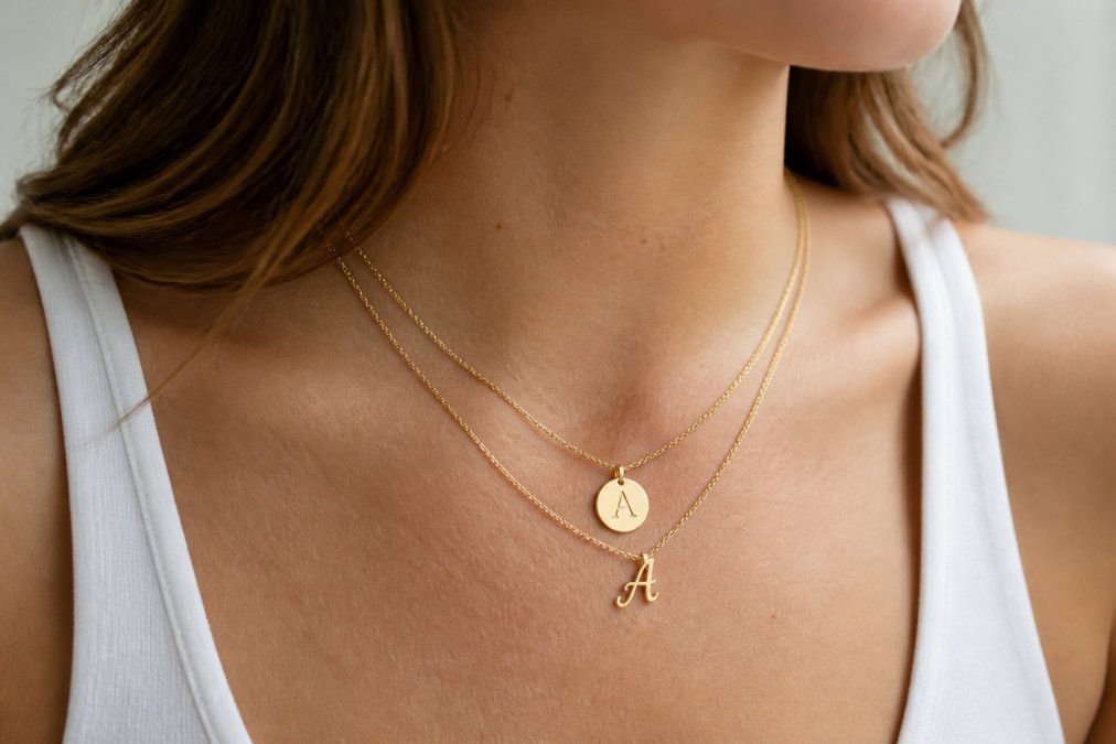 Woman wearing two layered gold initial pendant necklaces in soft natural light against her collarbone