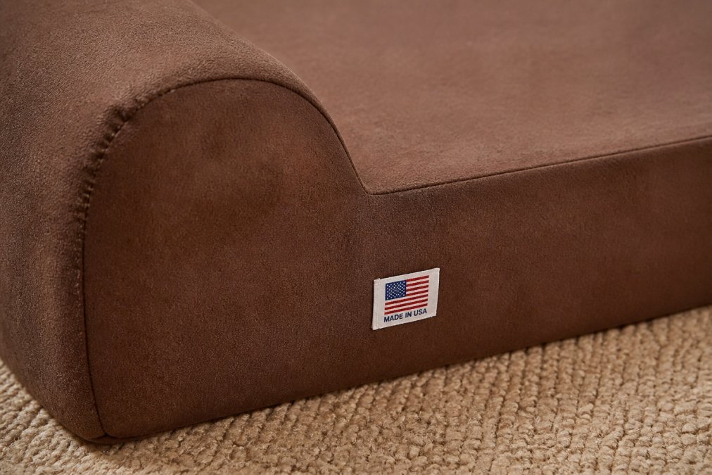Close-up of a premium orthopedic dog bed showing detailed stitching, high-quality microsuede fabric texture, and a visible "Made in USA" label sewn into the seam, with natural fabric showing superior craftsmanship