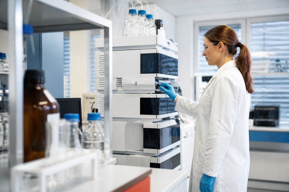 Laboratoriumtechnicus die aan een HPLC-apparaat werkt, met schermen die chromatogrammen en analyseresultaten tonen, in een moderne professionele onderzoeksomgeving met wit laboratoriummateriaal